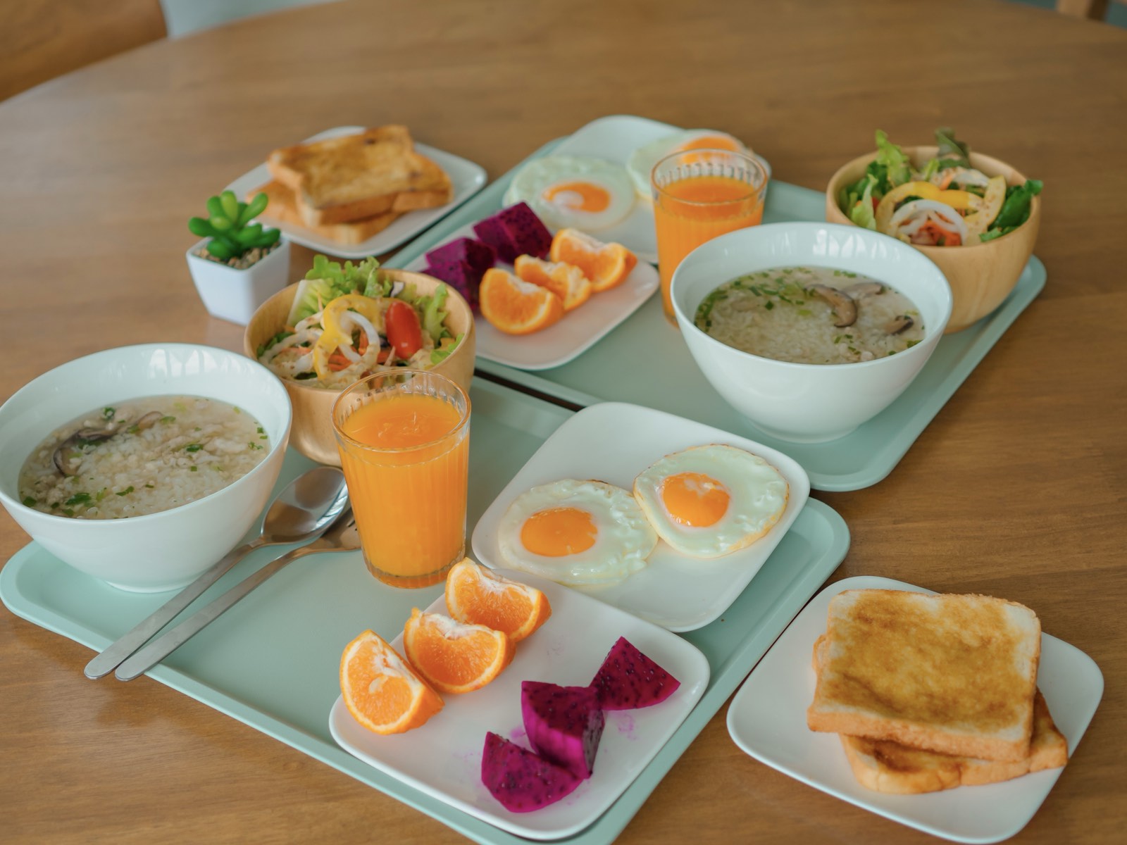 Breakfast sets with congee, eggs, toast, fresh fruit, and juice