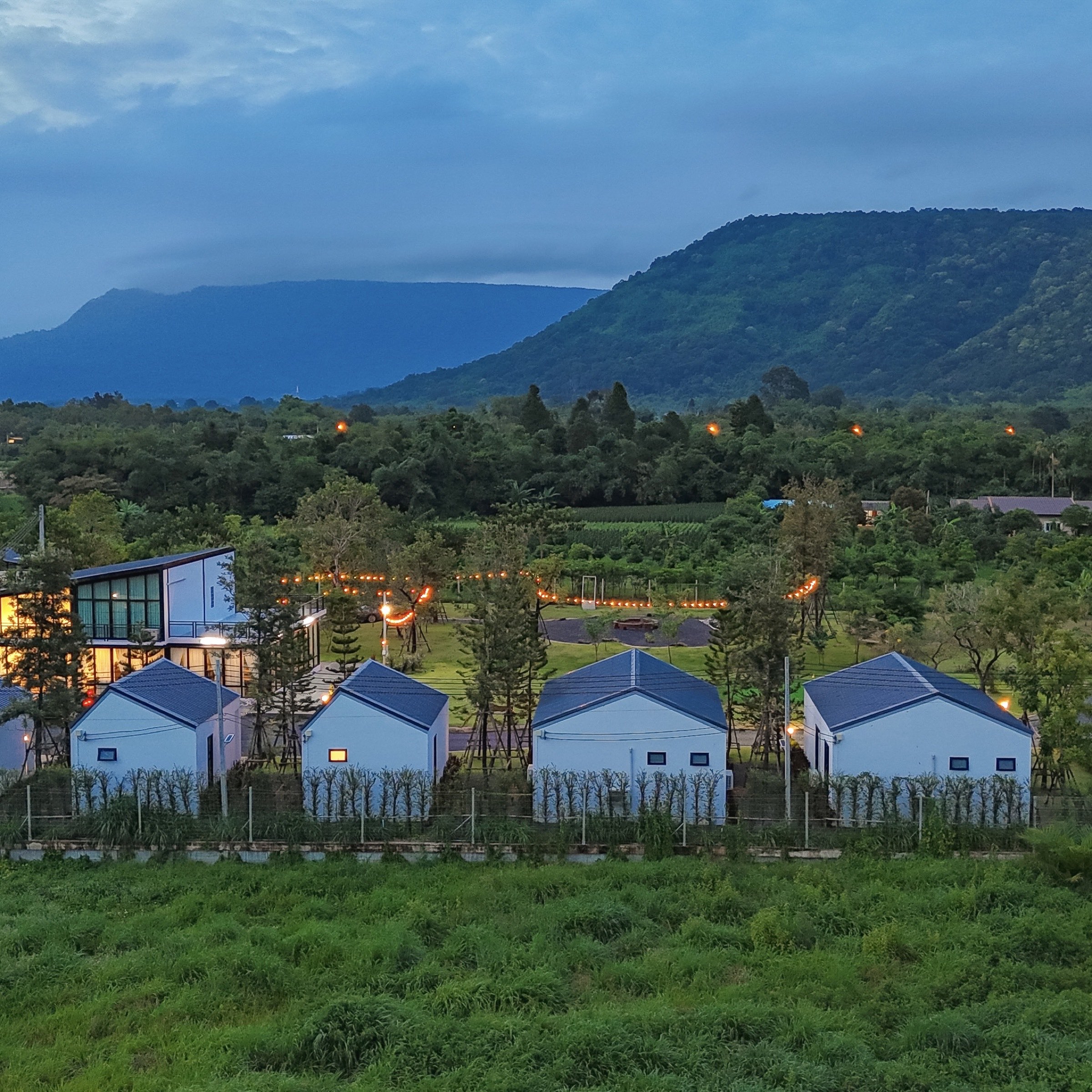 Twilight view of Myrrh Resort villas with string lights, surrounded by mountains