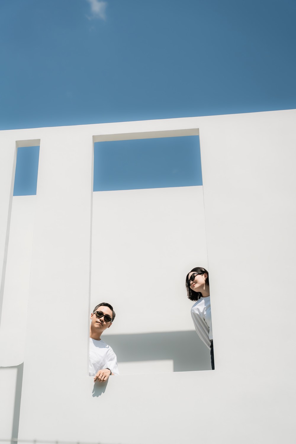Wedding couple framed by minimalist white wall openings against blue sky